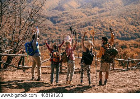 Hikers Standing On The Glade With Backs Turned And Hands Raised. Autumn Season, Adventure Concept.