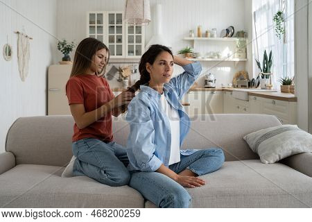 Teenage Girl Daughter Braiding Hair And Making Hairstyle For Her Attractive Charming Mother While En