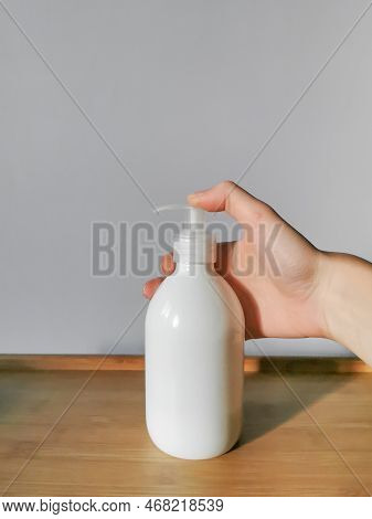 Woman's Hand Applying Body Lotion In White Dispensser Bottle On The Wooden Table. Demonstration Of H