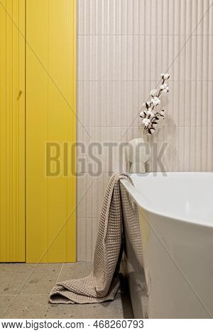 Modern Bright And Yellow Bathroom With Lamella Wall. Big White Bath With Btrown Towel And Dried Flow