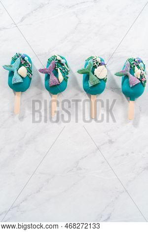 Mermaid Cakesicles With Drizzled Chocolate, Chocolate Mermaid Tails, Seashells, And Sprinkles.
