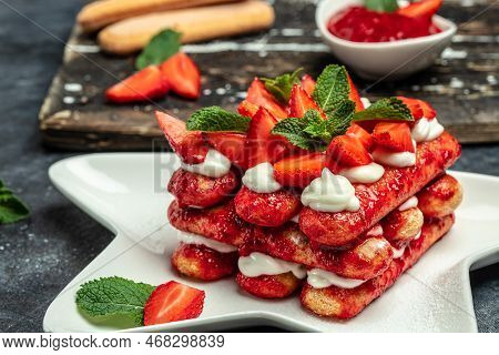 Italian Dessert Tiramisu Cake With Fresh Strawberry, Biscuit And Whipped Cream And Mint On A Dark Ba