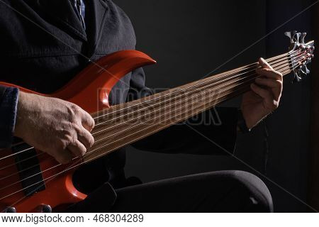 Male Musician Playing Six-string Fretless Bass Guitar On Dark Background