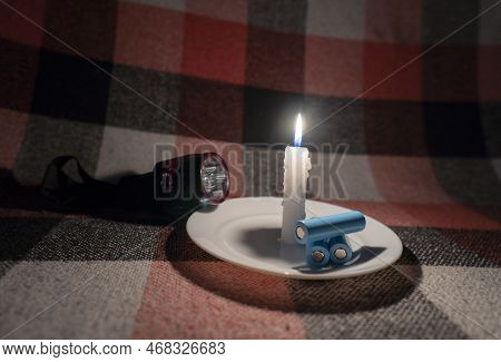 Three Discharged Cylindrical Batteries And A Headlamp Lie Near A Burning Candle (close-up). Power Ou