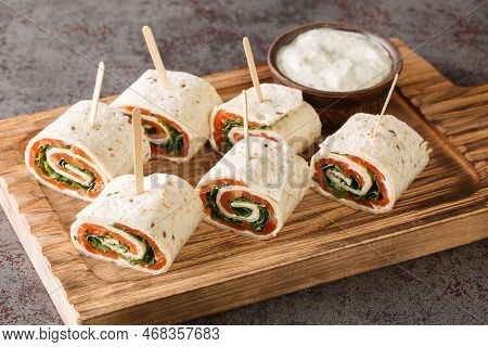 Rolls Of Thin Pancakes With Smoked Salmon, Cream Cheese, Arugula Closeup On The Board On The Table. 
