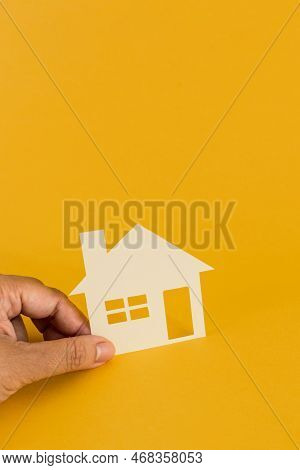 Female Hand Holding Paper House On Yellow Background. Family Home, Homeless Shelter, International D