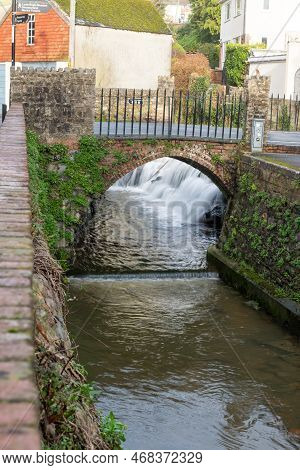 Long Exposure Of A Watefall Flowing Under A Bridge On The River Lim Walkway At Lyme Regis In Dorset.