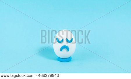 Lonely Egg With A Sad Expression Close Up. The Concept Of A Pessimistic Outlook On Life. Blue Backgr