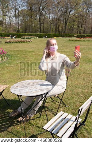 Young Woman In A Protective Mask Takes A Selfie With Blooming Sprimg Tulips