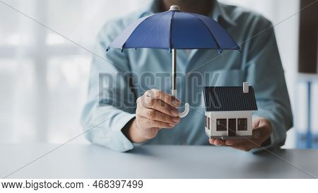 Individuals Holding Small Umbrellas And Model Homes, Housing Insurance Against Impending Loss And Fi