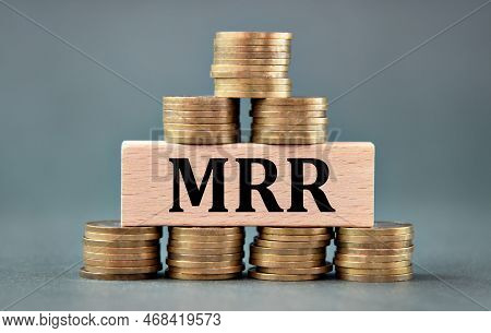 Mrr (monthly Recurring Revenue) - Acronym On A Wooden Bar Against The Background Of Stacks Of Coins.