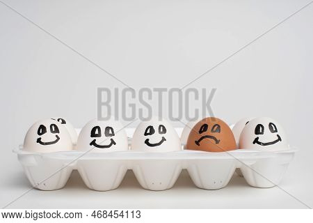 Tray Full Of Smile White Eggs And Only One Different Sad Orange Egg. Discrimination, Xenophobic, Rac