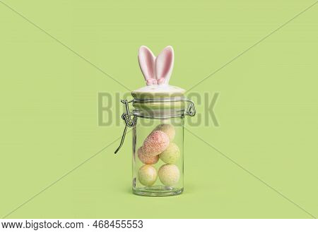 Easter Bunny Ears Sweets Glass Jar With Tiny Eggs Inside On Spring Yellow Green Edgeless Background.