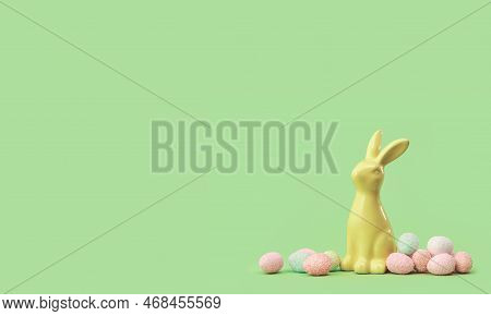 Yellow Easter Bunny With Many Tiny Eggs Sweets Around On Green Edgeless Background. Happy Easter Hol