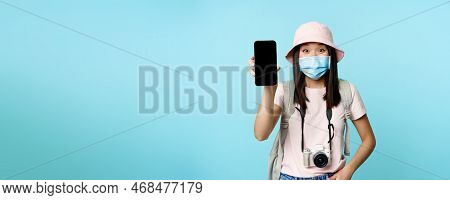 Enthusiastic Young Asian Woman In Medical Face Mask, Showing Mobile Phone App Interface, Tourism App