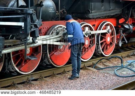 KIEV, UKRAINE - JAN 07, 2023: worker checks the mechanical parts of a retro steam locomotive wheelset on the Central Railway Station on January 07, 2023 in Kiev, Ukraine. 1st Railway Station opened in Kiev in 1868-1870 (project by architect Vishnevsky).