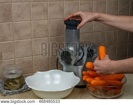 Close-up Of Female Hands Rubbing Red Ripe Carrots On An Electric Grater. Processing Of Ripe Fresh Ve