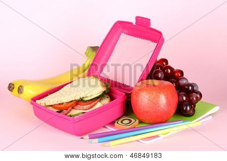 Madkasse med sandwich, frugt og brevpapir på pink baggrund