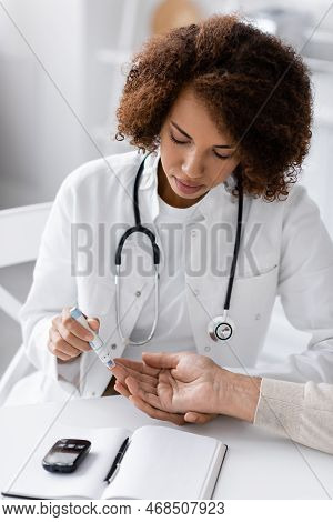 Curly African American Doctor Taking Blood Sample Of Mature Patient With Lancet Pen Near Glucose Met
