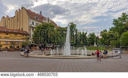 Szeged, Hungary - July 30, 2022: People Sitting Around Water Fountain At Dugonics Square In Front Of