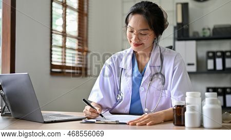 Professional Asian Female Doctor Or Pharmacist Working On Her Tasks At Her Desk In The Clinic Office