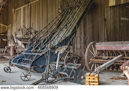Old Wooden House Wall With Ancient Tools And Stuff. Old Rusted Farm Machinery. Old Rusty Plow And Pl