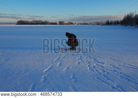Fisherman On Winter Fishing. A Man Sits Near A Hole In A Frozen Lake Waiting For A Bite. Snow On Ice