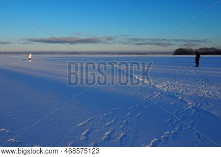 Fisherman And Fisherwoman On Winter Fishing. A Man Sits Near A Hole In A Frozen Lake And Waits For A