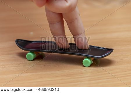 The Child\'s Fingers Ride On A Fingerboard, Wooden Surface, Close-up. Fingerskate Finger Training.