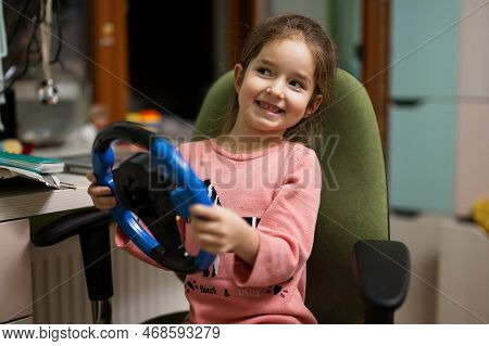 Girl Sitting On Chair With A Child's Steering Wheel In Her Hands In Children's Room.
