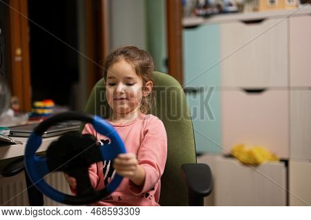 Girl Sitting On Chair With A Child's Steering Wheel In Her Hands In Children's Room.