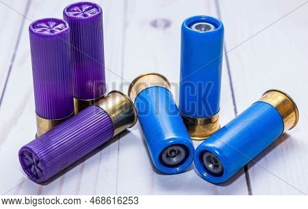 Six 12 Gauge Shotgun Shells, Three Purple Bird Shot And Three Blue Slugs On A White Wooden Backgroun