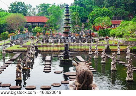 Ancient Water Palace Tirta Gangga With Fountains, Natural Pools, Path In Fish Pond With Statues Of D