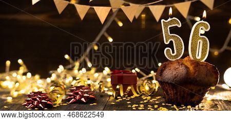 Number 56 Golden Festive Burning Candles In A Cake, Wooden Holiday Background. Fifty-six Years Since