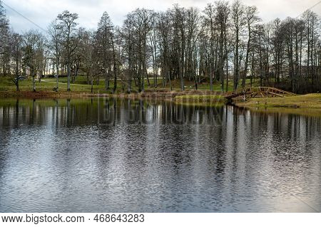 A Wooden Bridge From The Shore To A Small Island In The Lake In The Manor Park, Garsene, Latvia