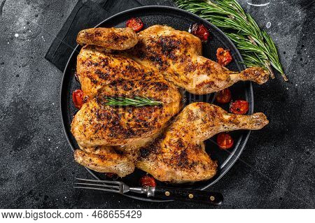 Tobacco Whole Chicken On Plate With Herbs And Tomato. Black Background. Top View.