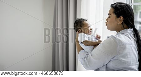 Asian Mother Holding A Baby Newborn Son S 2-month-old, Half-thai Half-nigerian, And Coaxing The Baby