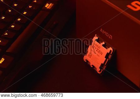 A Close-up Of An Amd Ryzen 9 3900X Processor In A Packaging Box With Backlit Keyboards In The Backgr