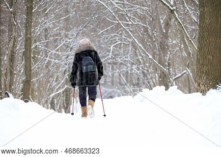Woman With Sticks Walks In Winter Park On Snow Covered Trees Background. Nordic Walking At Cold Weat