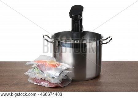 Sous Vide Cooker In Pot And Vacuum Packed Food Products On Wooden Table Against White Background. Th