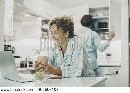 Young Adult Couple At Home In The Kitchen Busy In Indoor Leisure Domestic Activity Together. Woman W