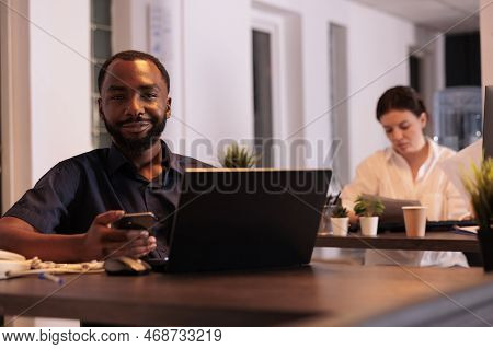 Smiling African American Man Working On Startup Project On Laptop, Using Smartphone Appplication In 