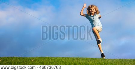Little Adorable Boy Running On Grass. Excited Kid Play The Green Grass. The Child Has Blond Long Hai