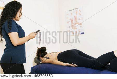 Professional Physiotherapist Electrostimulating A Lying Patient. Physiotherapist Electrostimulating