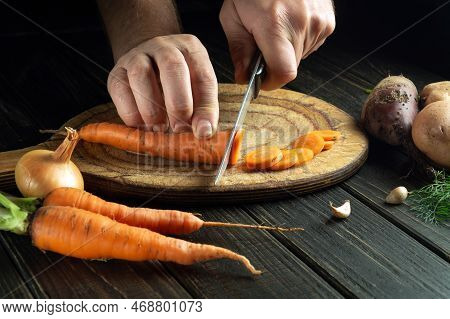 The Cook Cuts Fresh Carots On A Wooden Cutting Board. Close-up Of Chef Hands While Preparing Vegetar