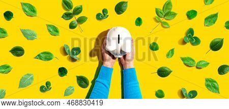 Person Holding A Piggy Bank With Green Leaves - Flat Lay