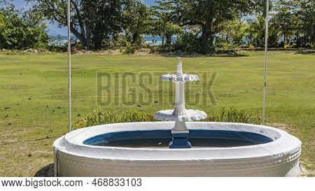 An Old Non-working Fountain In The Park, On A Green Lawn. The Stone Bowl Is Painted With White And B
