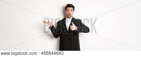 Portrait Of Hadnsome Bearded Man In Formal Suit, Showing Thumb-up And Holding Product In Hand Over W