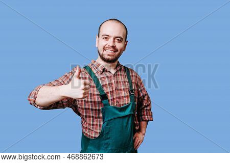 An Ebullient Young Farmer With A Beard Is Photographed In Overalls, Giving A Thumb Up And Standing I