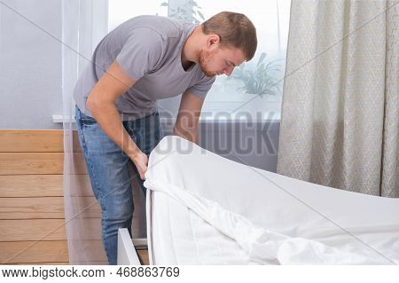 A Man Makes His Cozy Bed With Fresh Bright White Bed Linen. Making The Bed With Fresh Bed Linen By W